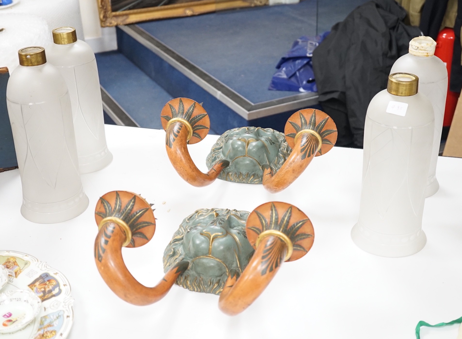 A pair of carved and decoratively painted twin-branch lion mask wall lights with tall glass shades, wall lights 38cms high, shades 32cms high